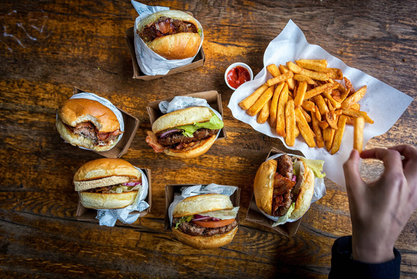 pacco di hamburger e patatine fritte su un tavolo di legno scuro con ketchup e una mano nell'immagine - Foto, immagini
