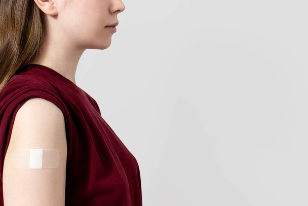 Neznámá žena v tričku s náplastí na rameni po koronavirové vakcíně, šedé pozadí, kopírovací prostor. Očkování, imunizace, koncepce prevence chřipky. Jak získat vakcínu Covid-19 - Fotografie, Obrázek