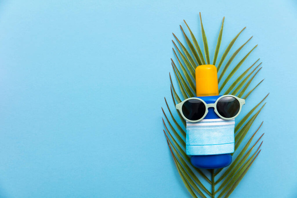 Coronavirus summer vacation background. Sun cream with sunglasses and face mask - Valokuva, kuva