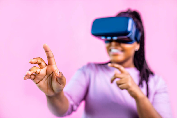 dark skinned woman sing glasses of virtual reality on pink studio background - Photo, Image