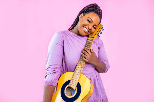Young woman playing guitar on color pink studio background - Foto, afbeelding