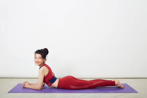 Evdeki yoga minderinde kobra pozu veren güzel bir Asyalı kadın, sağlıklı yaşam ve zihinsel gelişim arasındaki doğal denge kavramı. - Fotoğraf, Görsel
