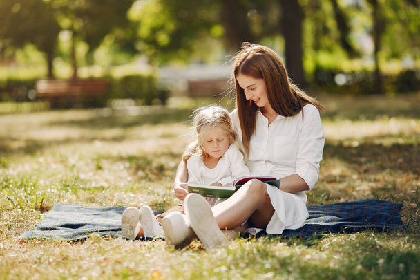 Mother with little daughter sitting on a plaid and read the book - Φωτογραφία, εικόνα