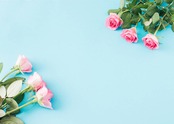 Twee boeketten van roze rozen takken diagonaal gerangschikt op een lichtblauwe achtergrond met een plaats voor een bericht. - Foto, afbeelding