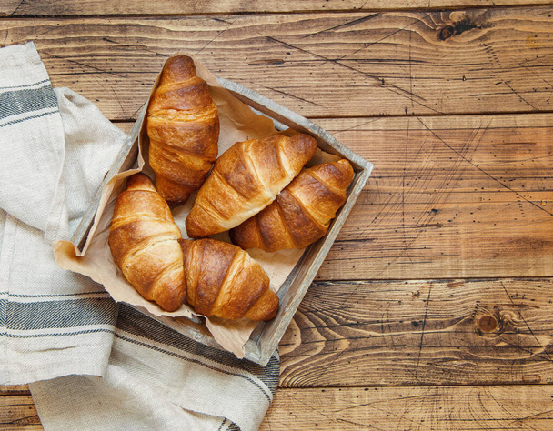 Fresh croissants in a wooden tray with a kitchen towel on a wooden table top view - Photo, Image