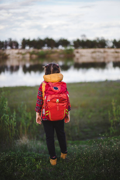 Rear view of a little girl hiker staying with backpack in front of the river - Fotografie, Obrázek