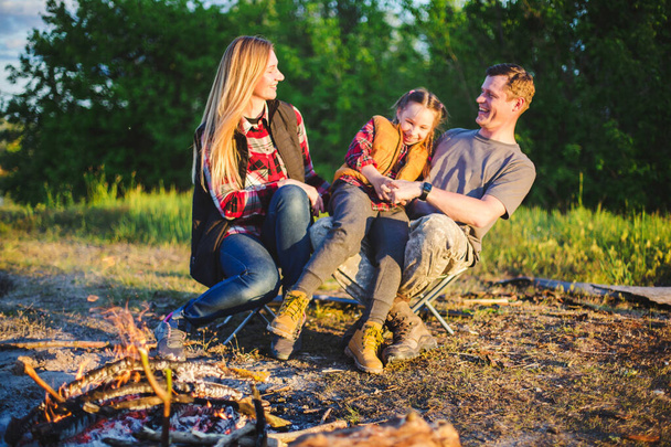 Young family traveling and camping, having fun with a child in front of campfire at sunset  - Foto, immagini