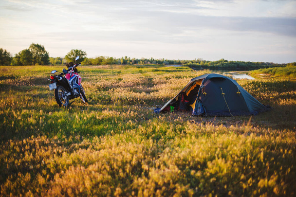 A tent and a motorbike on the bank of Desna River at sunset - Foto, imagen