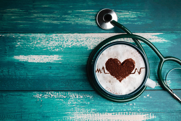 Maailman terveyspäivä. Terveydenhuolto kahvi rakastaja ja sydänsairaus käsite. Latte Art by Cinnamon päälle kuin sydän muoto ja pulssi syke. Kuuma kahvikuppi makaa pöydällä sisällä stetoskooppi. Ylhäältä - Valokuva, kuva
