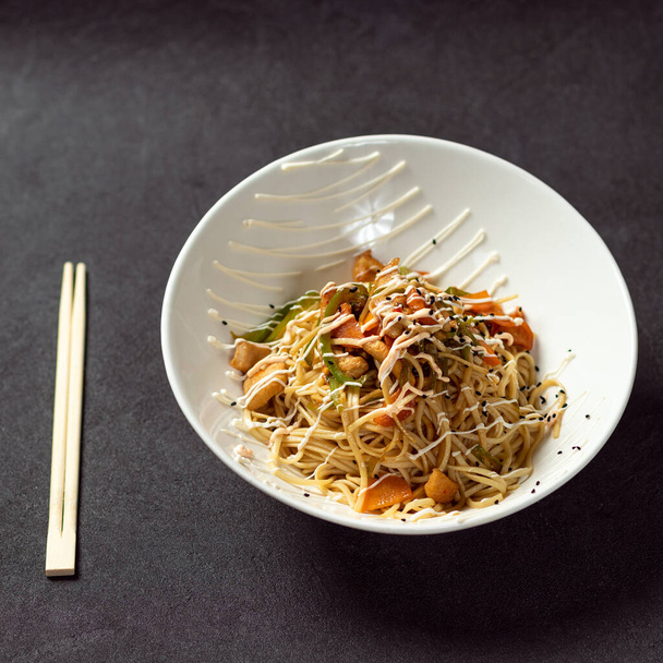 Chow mein noodles and vegetables dish with wooden chopsticks on the black background - Photo, Image