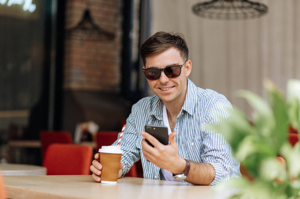 Handsome brunet man sitting in a cafe smiling and looking at the phone - Fotoğraf, Görsel