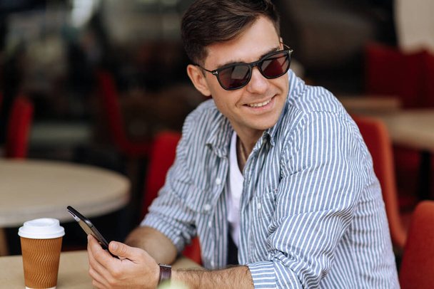 Handsome brunette man in sunglasses looking to the side while sitting in a cafe - Фото, изображение