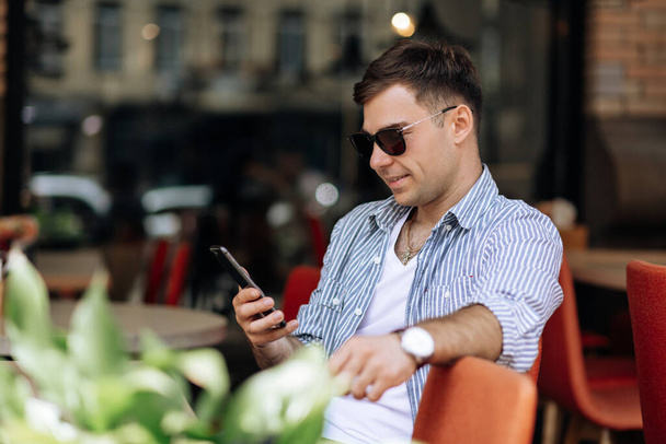 Handsome brunet man in sunglasses smiling into the phone while sitting in a cafe - 写真・画像