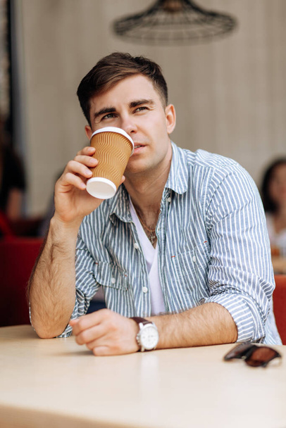 Handsome brunette man drinking coffee in a cafe on a warm summer day - 写真・画像