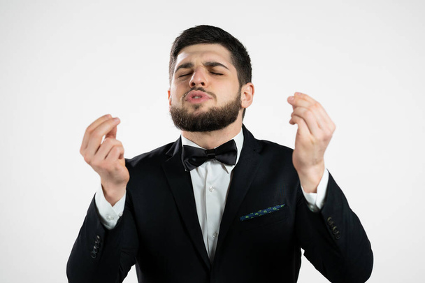 Young man making delicious, perfect gesture. gentleman with beard in tuxedo admires taste of italian food on white studio background. Bellissimo concept. - Foto, Bild