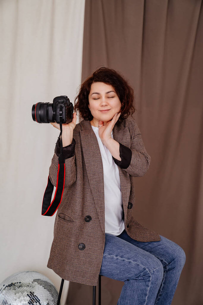 donna in jeans e giacca a scacchi sul seggiolone in studio fotografico con macchina fotografica - Foto, immagini