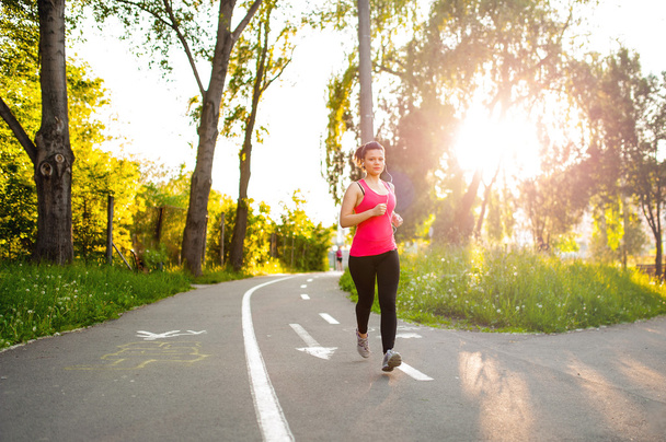Portrait of a smiling active female runner, resting from jogging in park at sunset - 写真・画像