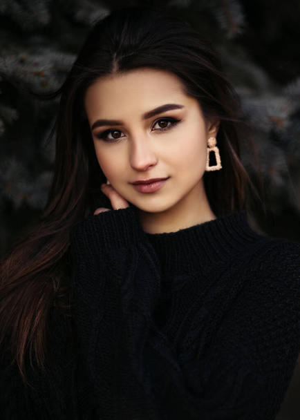 Vertical lifestyle portrait of young indian woman standing near fir tree dressed in black pullover and looking at the camera.  - Fotoğraf, Görsel
