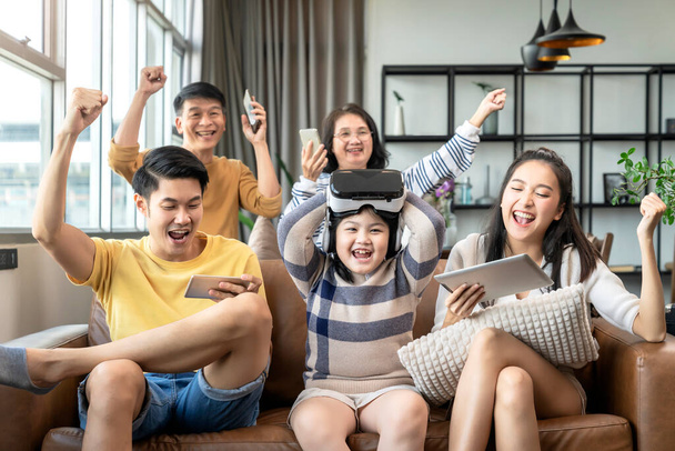 smart technology with lifestyle at home,asian generation family enjoy technology device hand use smartphone tablet and vr goggle glasses play fun together on sofa living room at home quarantine moment - Photo, image
