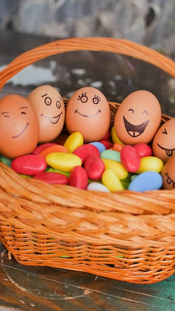 Стек яєць з намальованими руками на солом'яному кошику з різнокольоровими цукерками, підготовкою до Великодня, концепціями святкового настрою
 - Фото, зображення