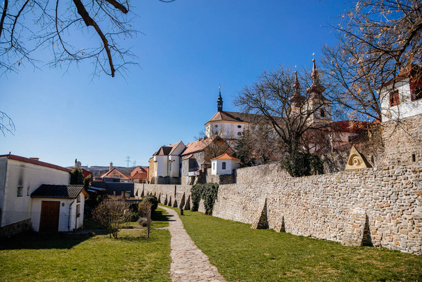 Middeleeuwse gotische stadvesting, vestingmuur op zonnige dag op de top van de heuvel, oude vesting, antieke metselarij, Kerk van Verheffing van het Heilig Kruis, Kadan, Tsjechië, 04 april 2021 - Foto, afbeelding