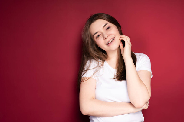 Beautiful woman in braces smiling happily tilting her head to one side while standing on red background - Фото, изображение