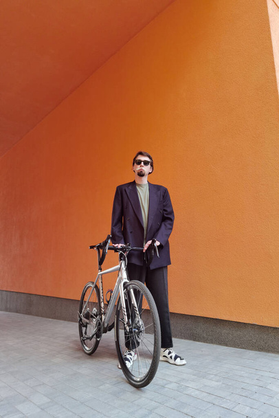 Portrait of beautiful adult man with bicycle on orange background. - Φωτογραφία, εικόνα