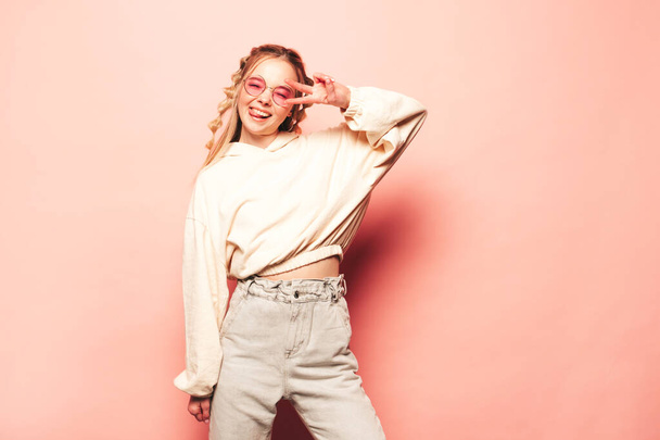 Portrait of young beautiful woman looking at camera.Trendy female smiling in casual summer hipster clothes. Positive and funny model posing near pink wall in studio in sunglasses.Happy and cheerful - Foto, Imagen