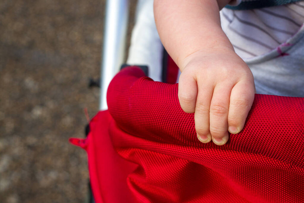 La mano de un niño pequeño agarrándose fuerte: sujetándose a un buggy rojo - Foto, Imagen