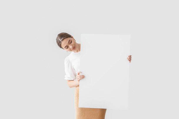 Beautiful young woman with blank poster on light background - Фото, зображення