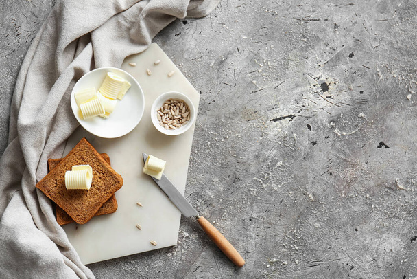 ломтики свежего хлеба, масла и семян подсолнечника на сером фоне - Фото, изображение