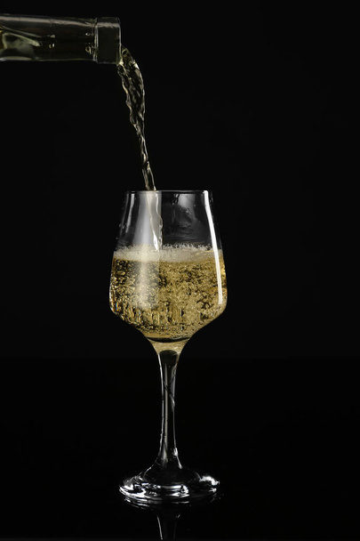 Gieten van wijn uit fles in glas op donkere achtergrond - Foto, afbeelding
