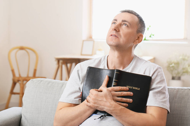 Uomo con Bibbia seduto sul divano di casa - Foto, immagini