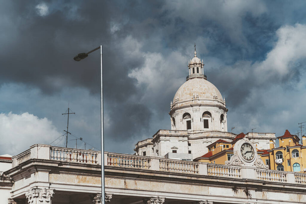 View of The Church of Santa Engracia or another name National Pantheon, with a beautiful partly stormy cloudscape in the background and a building of the military museum with a clock in the foreground - Fotoğraf, Görsel