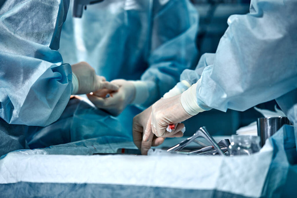 Hände eines Chirurgenteams in Nahaufnahme im Operationssaal während der Operation, sterile Instrumente liegen auf dem Tisch im Operationssaal. - Foto, Bild