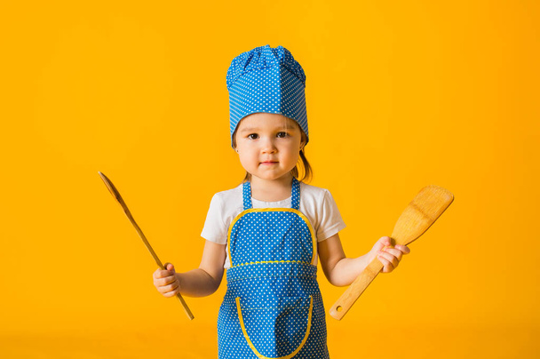 portrait d'une petite fille en costume de cuisinier tenant des cuillères en bois sur un fond jaune avec espace pour le texte - Photo, image