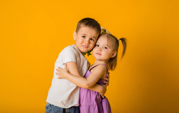 Küçük bir oğlan ve bir kızın portresi sarı bir arka plana sarılıp mesajlaşmak için yer açıyor. - Fotoğraf, Görsel