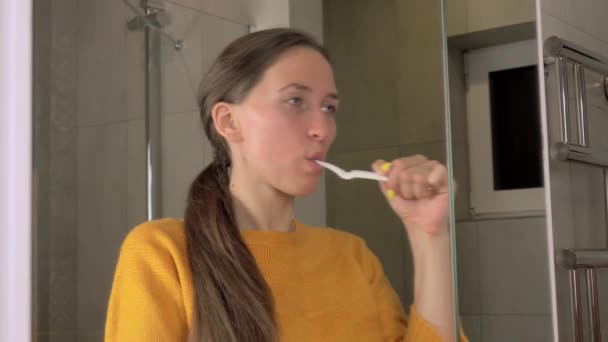 donna si riflette nello specchio si lava i denti con spazzolino e dentifricio - Filmati, video