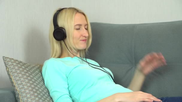 une femme heureuse se repose sur un canapé confortable, écoutant de la musique avec des écouteurs, - Séquence, vidéo