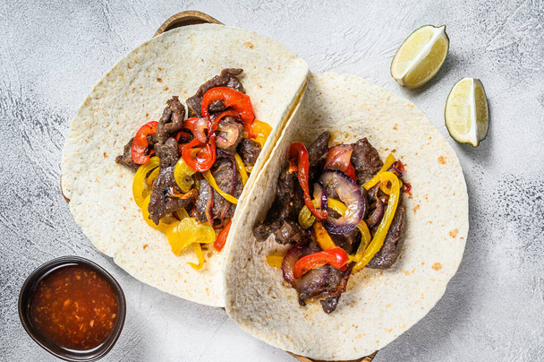 Fajitas with beef meat stripes, colored bell pepper and onions, served with tortillas and salsa. White background. Top view - Photo, Image