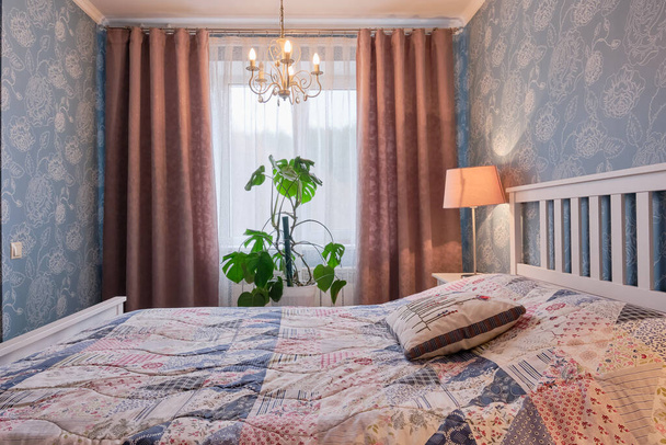 Interior of bedroom. Bed, pillows, lamp, curtains and houseplant near window - Valokuva, kuva