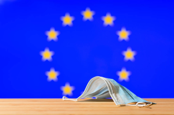 Tegen de achtergrond van de EU-vlag ligt een medisch masker op tafel. Het concept van een verplichte maskerregeling voor ingezetenen en toeristen uit de EU-landen tijdens een pandemie. - Foto, afbeelding