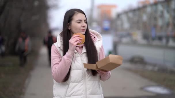 Mujer bonita caminando al aire libre en la ciudad y comiendo hamburguesa - Metraje, vídeo