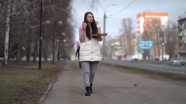 Ładna kobieta spaceruje po mieście i je hamburgery - Materiał filmowy, wideo