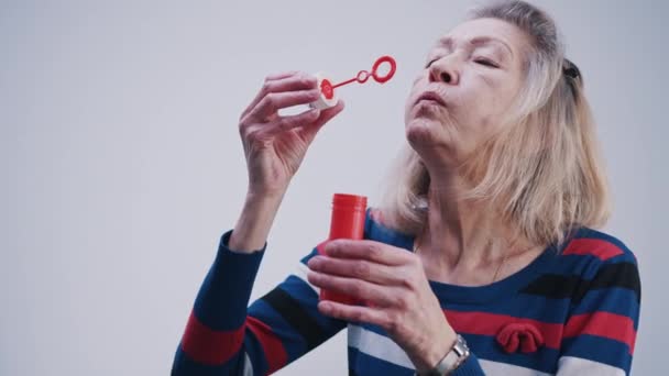 Elderly woman blowing soap bubbles indoors - Footage, Video