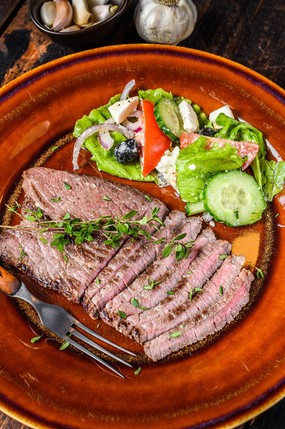 Жареная говядина мясной отбивной круглого стейка на тарелке с салатом. Темный деревянный фон. Вид сверху - Фото, изображение