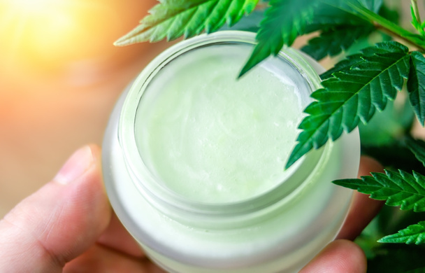 Hand hält Cannabis CBD Lotion Creme gegen Marihuana-Pflanze - Foto, Bild