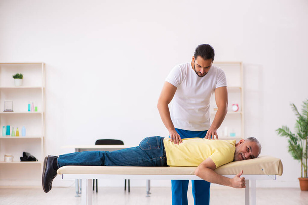 Old male patient visiting young male doctor chiropractor - Foto, Imagen