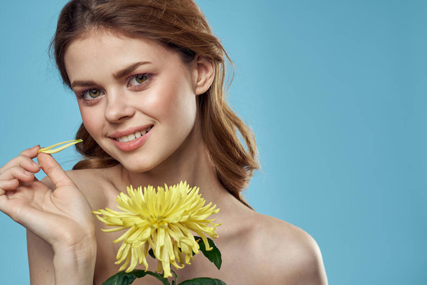 piękna kobieta z żółtym kwiatem w pobliżu twarzy uśmiechnięty przycięty widok portret nagie ramiona - Zdjęcie, obraz
