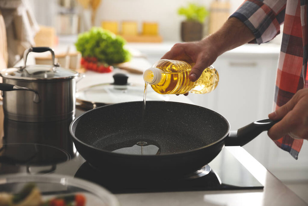 Man pouring cooking oil into frying pan in kitchen, closeup - 写真・画像